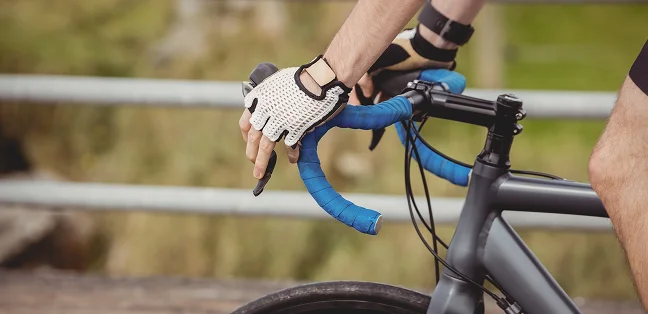 A cyclist wearing sports gloves and holding the handlebars of a road bike, riding on a road with a metal barrier in the background